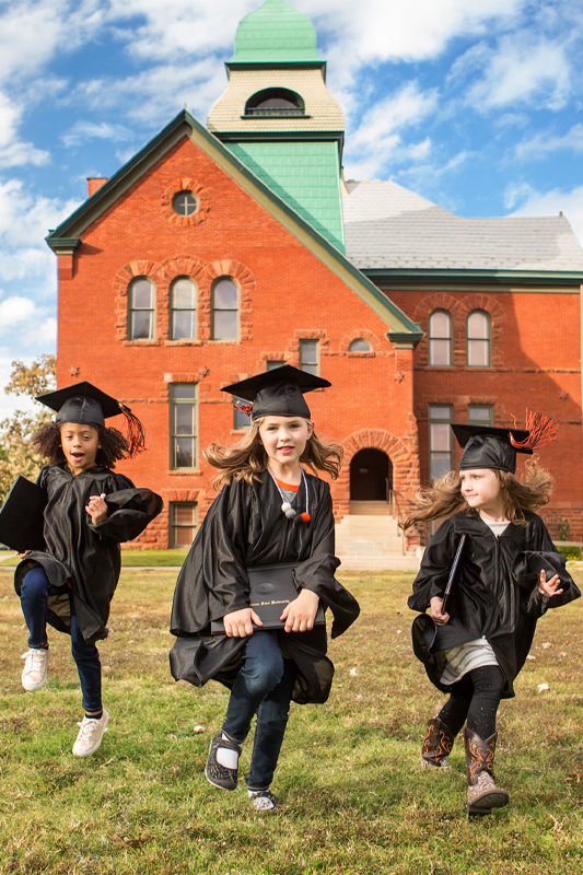 3 kids in graduation gowns in front of Old Central